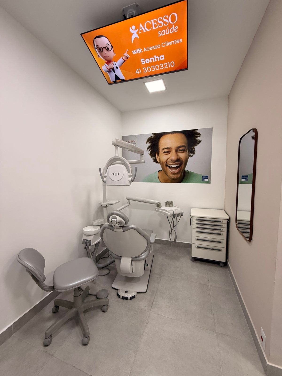 Consultório com TV de teto exibindo WiFi e dados da clínica — Acesso Saúde CIC